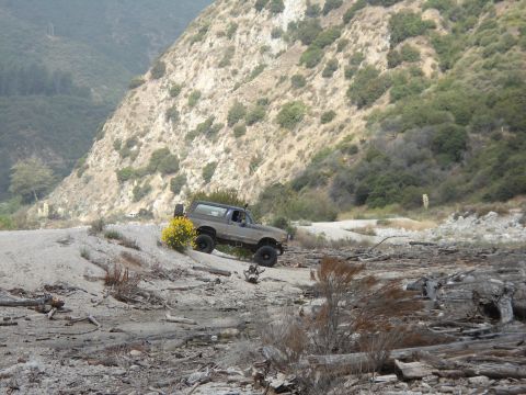 1994 Ford Bronco - A brown Ford Bronco navigates a rocky, off-road trail with a steep, vegetated hillside in the background.