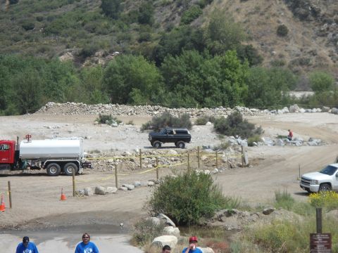 1994 Ford Bronco - A black SUV is parked in a dusty, outdoor area with a water truck and a white pickup truck visible.