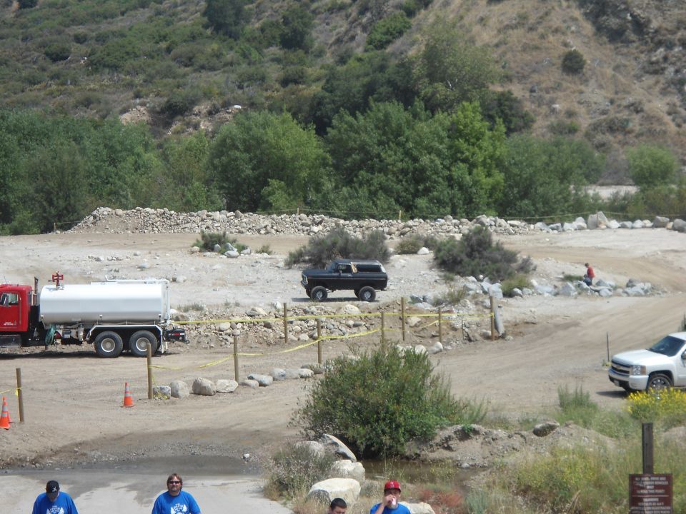 Black SUV parked on dirt road with water truck and white pickup nearby