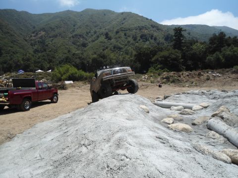 1994 Ford Bronco - Modified off-road truck navigates a rocky obstacle course with a red pickup truck nearby.