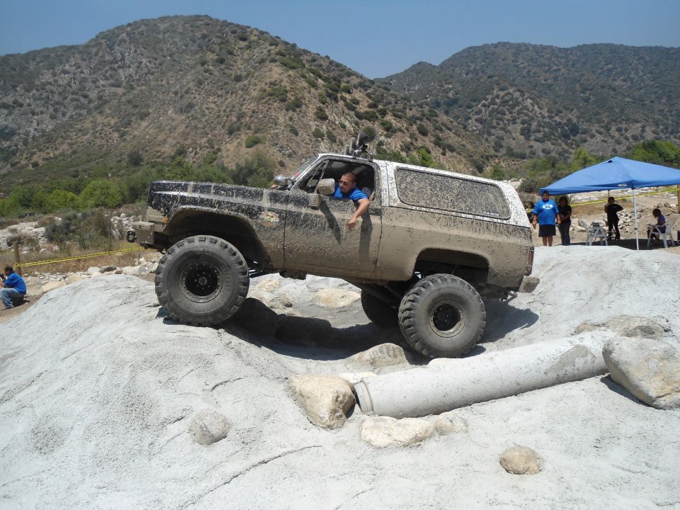 Mud-covered 1980s SUV with large tires navigating rocky terrain