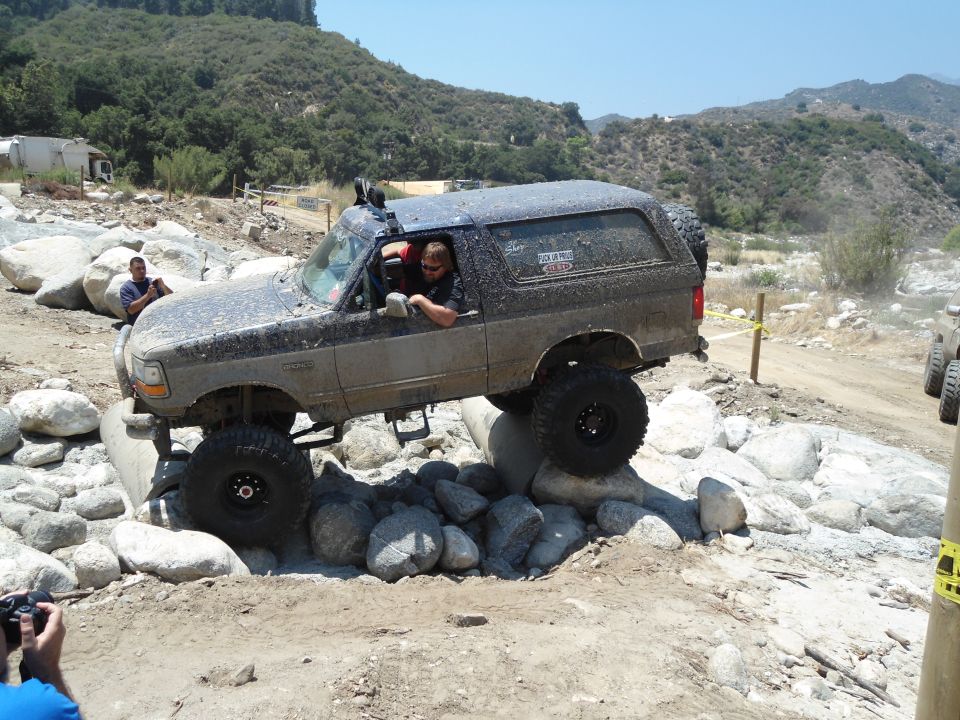 Mud-covered 1992 Ford Bronco navigating a rocky terrain, driver visible