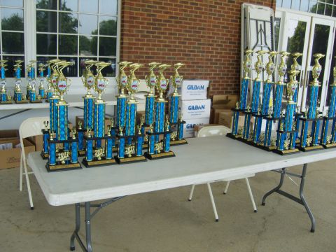2007 Ford Mustang - Numerous trophies are displayed on tables outside a brick building, with '2011' visible on the bases of many awards.