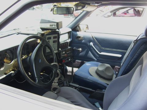 2007 Ford Mustang - The interior of a police car is shown, a radar gun, handcuffs, and a hat on the passenger seat. Another vehicle is visible through the wind…