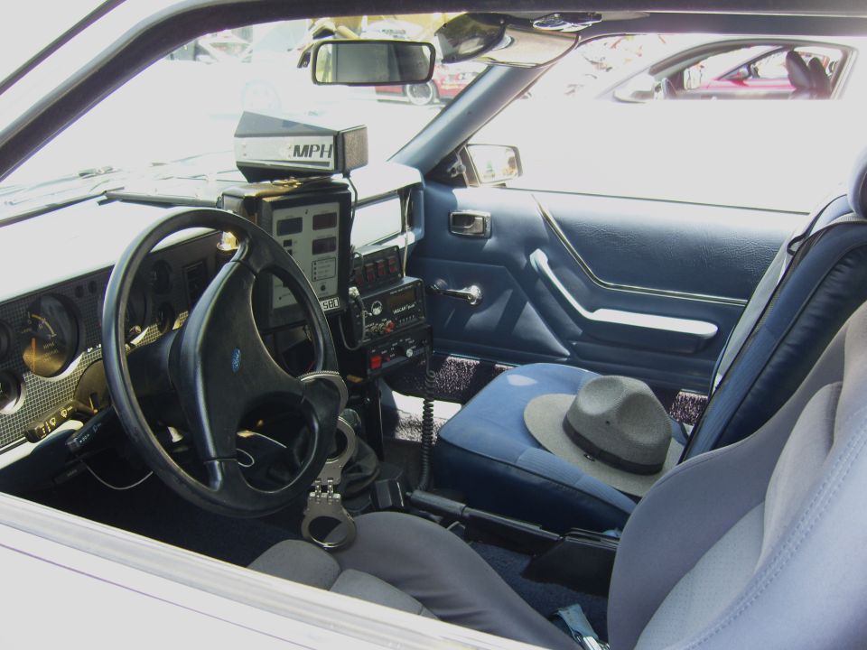 Interior of a police car with radar gun, handcuffs, and a hat on the passenger seat