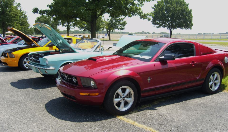 Red 2007 Ford Mustang parked in a line with other Mustangs, hoods up on some