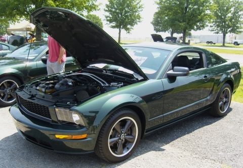 2007 Ford Mustang - A dark green 2007 Ford Mustang is displayed with its hood open, revealing the engine compartment. Another Mustang is visible in the backgro…