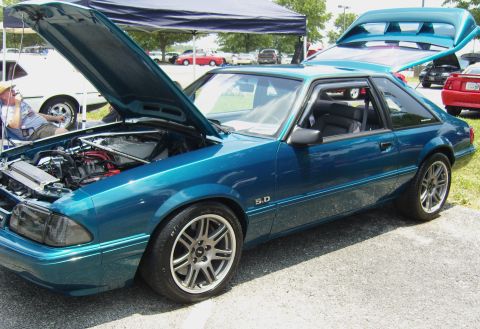 2007 Ford Mustang - A teal Ford Mustang from the 1990s is displayed with its hood and trunk open at an outdoor event.