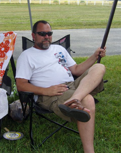 2007 Ford Mustang - A man relaxes in a camping chair under a canopy, holding a long pole.