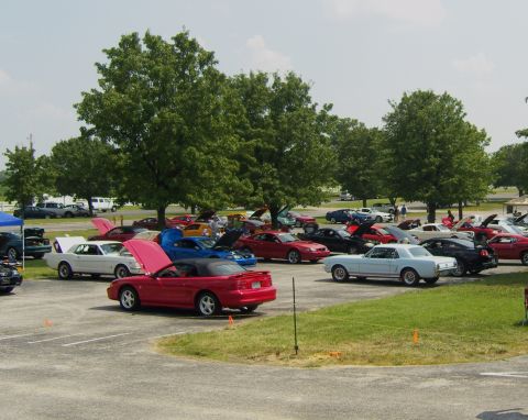 2007 Ford Mustang - A gathering of various cars are parked in an outdoor lot under a partly cloudy sky.