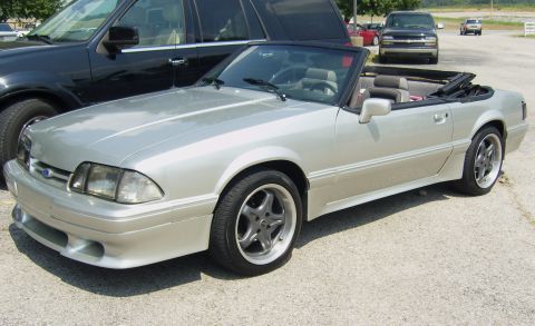 2007 Ford Mustang - A silver convertible is parked outdoors next to a black SUV, with other vehicles in the background.