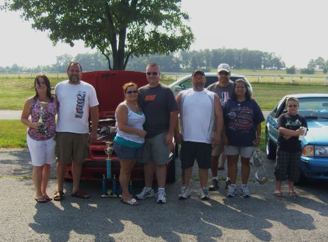 2007 Ford Mustang - A group of people stand with a red car and a blue car at an outdoor event.