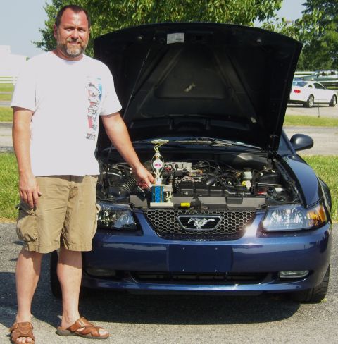 2007 Ford Mustang - A man proudly displays a trophy next to his blue Ford Mustang, which has its hood open, revealing the engine.