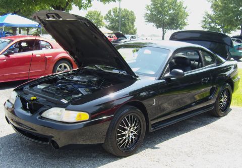 2007 Ford Mustang - A black Ford Mustang is parked with its hood open, alongside another Mustang.
