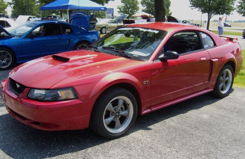 2007 Ford Mustang - A red 2007 Ford Mustang GT is seen at an outdoor car show, with another Mustang visible behind it.