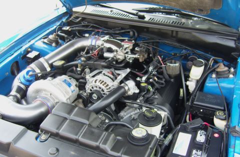 2007 Ford Mustang - Close-up view of a modified V8 engine with a prominent supercharger and custom intake piping.