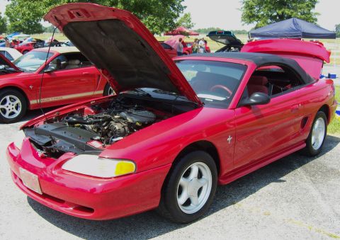 2007 Ford Mustang - A red convertible Mustang is displayed with its hood and trunk open, revealing the engine and interior. Another red Mustang is visible in t…
