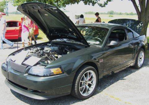 2007 Ford Mustang - A dark green Mustang is displayed with its hood open, revealing the engine bay. Another vehicle is parked nearby.