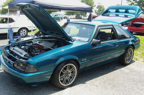 2007 Ford Mustang - A teal coupe with its hood and trunk open, displaying its engine and rear spoiler at an outdoor car show.