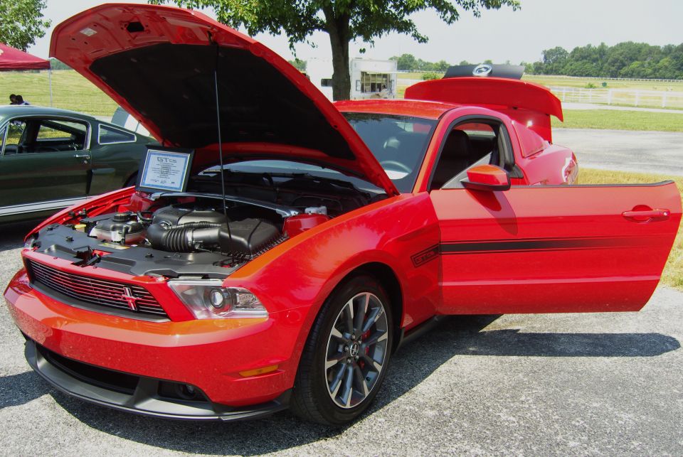 Red Ford Mustang GT with hood and driver door open, showing engine and interior
