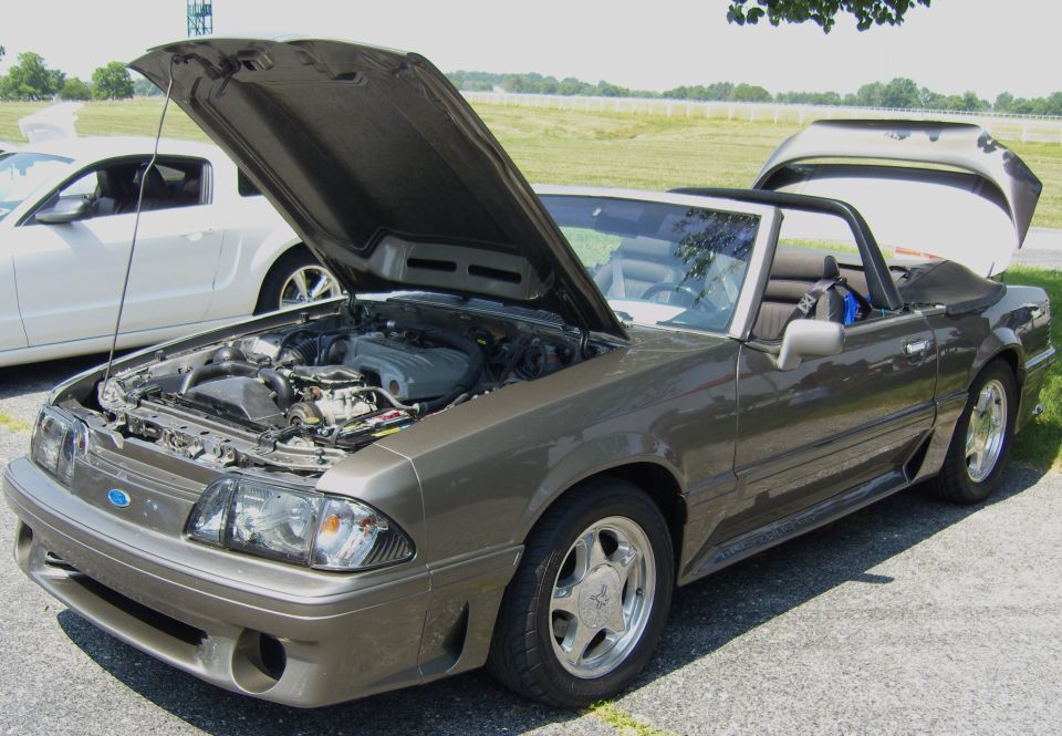 Brown 1990 Ford Mustang convertible, hood and trunk open, parked next to a white car