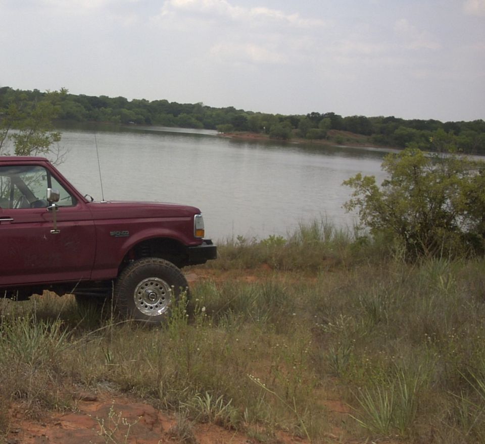 Front half of a lifted maroon Ford Bronco parked on grass beside a lake