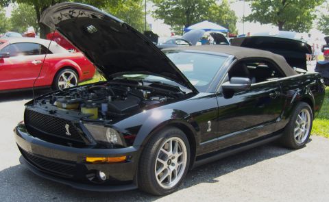 2007 Ford Mustang - A black convertible Mustang is displayed with its hood open, parked alongside another Mustang at an outdoor event.