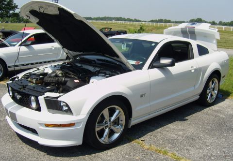2007 Ford Mustang - A white Ford Mustang GT is parked with its hood and trunk open, displaying racing stripes and chrome wheels.