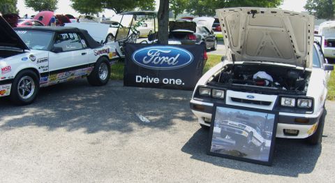 2007 Ford Mustang - A white Ford Mustang from the 1980s is displayed with its hood open, alongside a framed photograph of a similar vehicle.