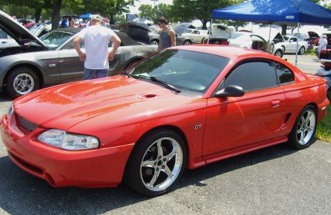 2007 Ford Mustang - Red Ford Mustang GT coupe with aftermarket wheels at a car show.