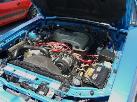 2007 Ford Mustang - The engine bay of a blue 1987 Ford Mustang is visible, with a red Mustang parked nearby.