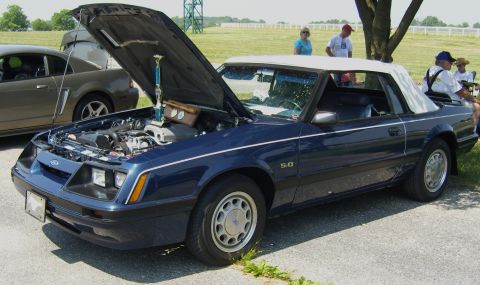2007 Ford Mustang - This blue convertible Mustang, likely from the late 1980s, displays a prominent 5.0 badge and has its hood open, revealing the engine bay.