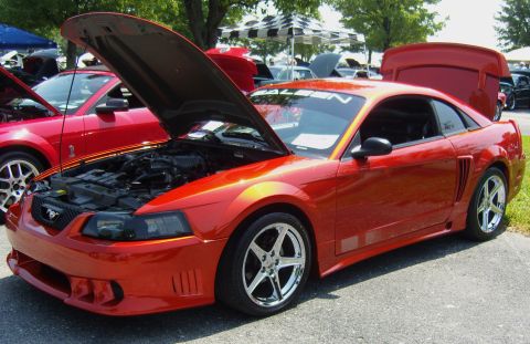 2007 Ford Mustang - Orange SN95 New Edge Ford Mustang coupe on display with hood and trunk open, wearing a Saleen-style body kit with side scoops, tall rear wi…