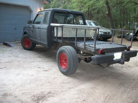 1994 Ford Explorer - A modified pickup truck with a flatbed and red wheels sits in a sandy driveway.