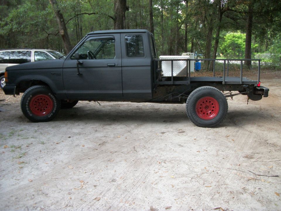 Dark gray pickup truck with red wheels and a flatbed conversion, seen from the side