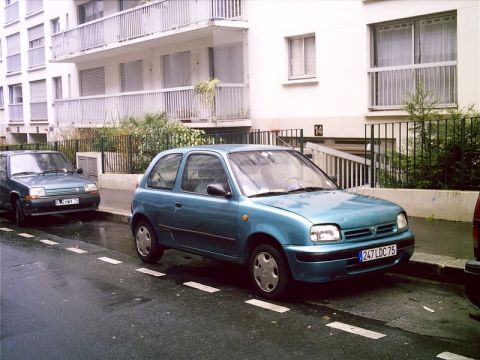 1991 Ford LTD Crown Victoria - A teal Nissan Micra hatchback is parked on a wet street next to a Renault 5. The car appears to be from the mid-1990s.