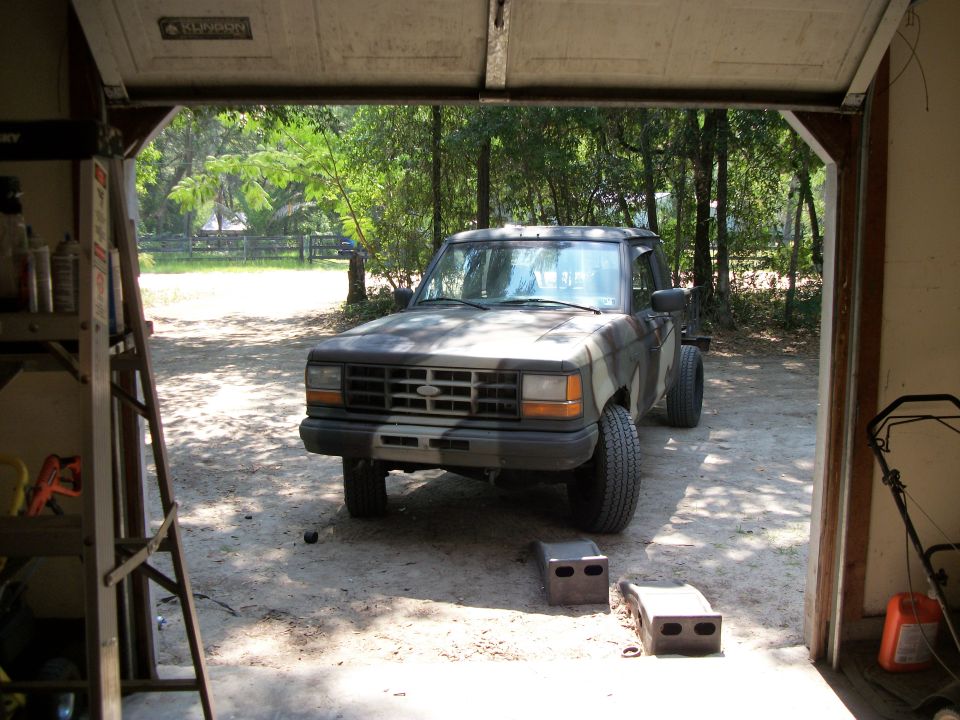 Camouflaged pickup truck parked in an open garage. The truck has a Ford emblem on the grille