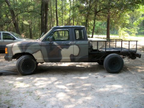 1994 Ford Explorer - This modified Ford Ranger pickup truck features a custom flatbed and camouflage paint job, seen parked in a wooded area.