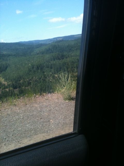 2005 Jeep Wrangler - View of forested hills and sky from inside a vehicle, with a gravel road visible.