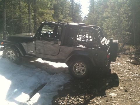 2005 Jeep Wrangler - A black Jeep Wrangler is parked on a dirt and snow-covered trail in a forest.