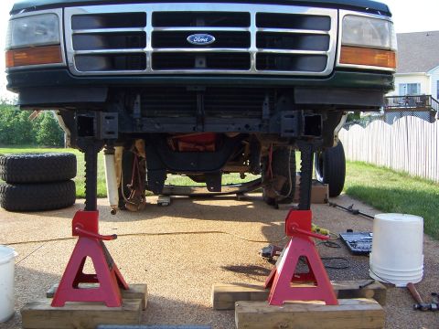 1992 Ford Bronco - Front view of a green Ford truck, lifted on jack stands for maintenance, revealing its undercarriage and grille.