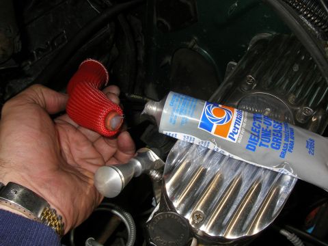 1990 Ford Bronco - A hand holds a red spark plug wire boot next to a tube of dielectric grease, with engine parts visible in the background.