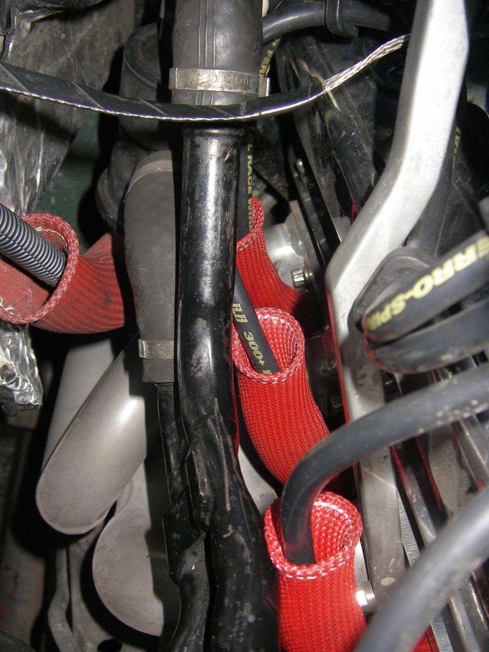 Close-up of engine bay hoses with red protective sleeves and black wiring. Text 'RACE 300+' visible on one hose