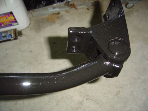 1986 Ford Bronco - A close-up view of a freshly painted metal bracket, likely a vehicle part, resting on a concrete floor.