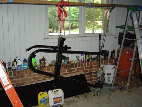 1986 Ford Bronco - A spare tire carrier assembly is suspended by a hoist in a garage setting, with various automotive fluids and tools nearby.