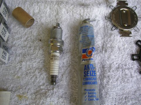 1990 Ford Bronco - A single spark plug, a tube of anti-seize lubricant, and a spark plug gap tool are laid out on a white towel.