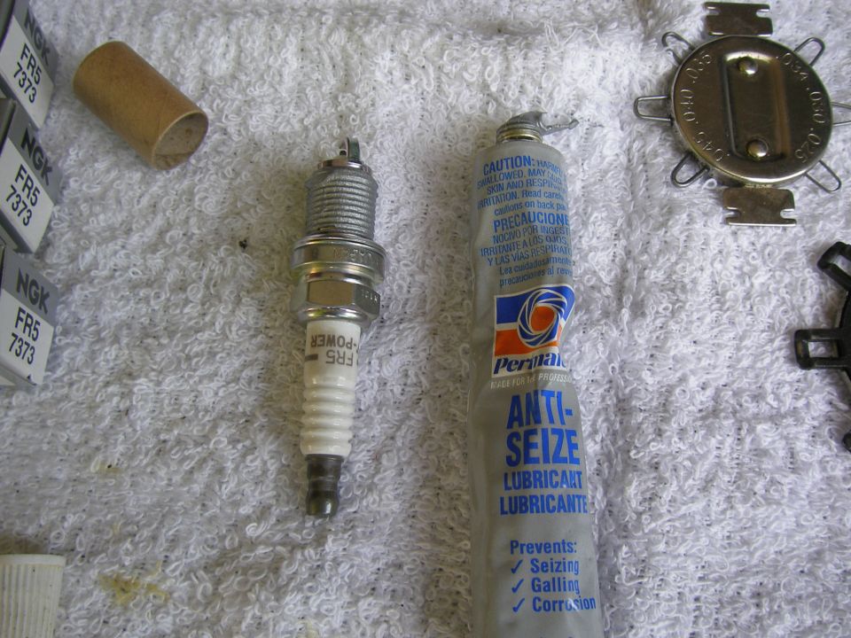 Spark plug, tube, anti-seize lubricant, and a gap tool on a white towel