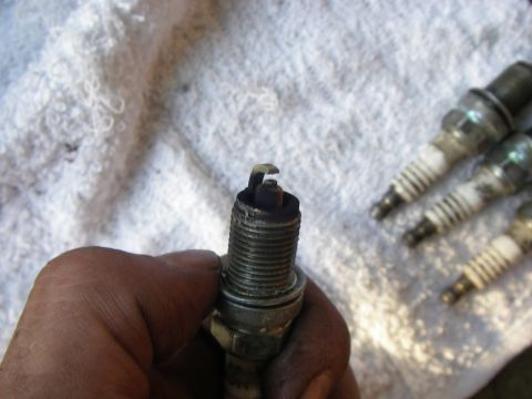 1990 Ford Bronco - Close-up of a used spark plug being held, with other spark plugs visible in the background.