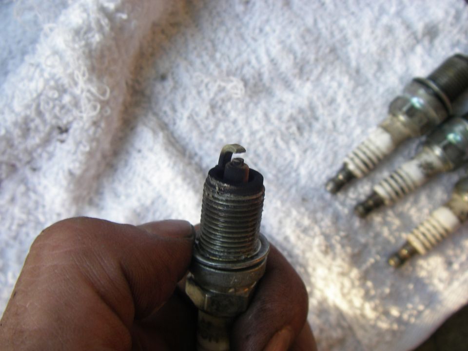 Spark plug held in hand, with three others blurred in background on white cloth