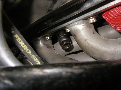 1990 Ford Bronco - Close-up of a spark plug being serviced on an engine's exhaust manifold, with part of a "FERRO-SP" labeled cable visible.